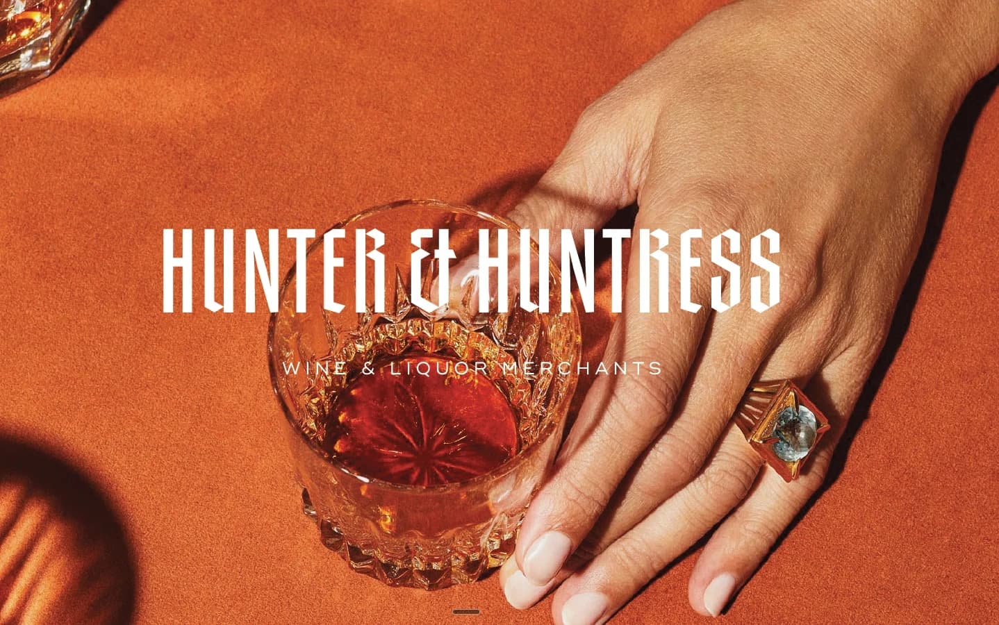 Hunter & Huntress branded glass and hand detail on a styled amber background, "Wine & Liquor Merchants"